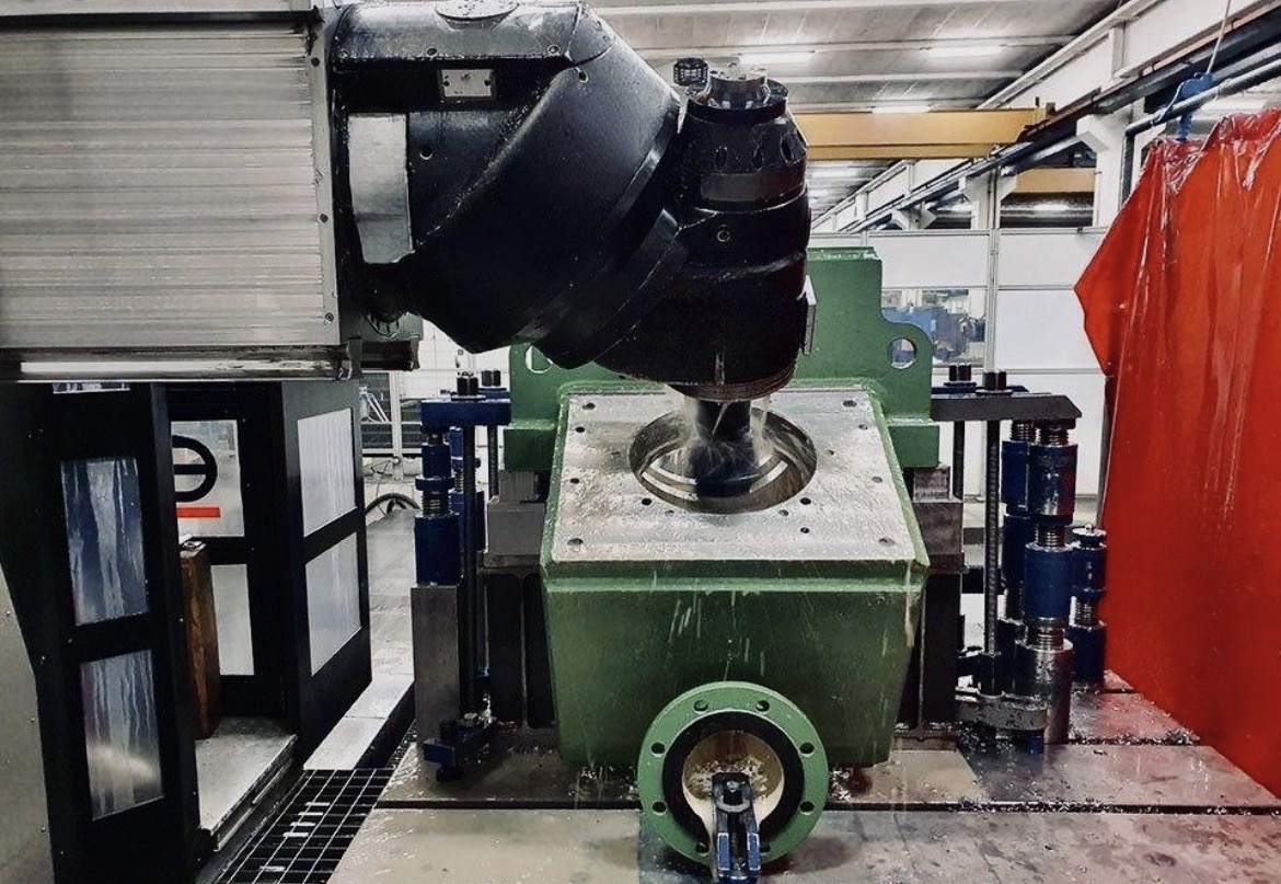 Five-axis milling head machining a large green cast housing